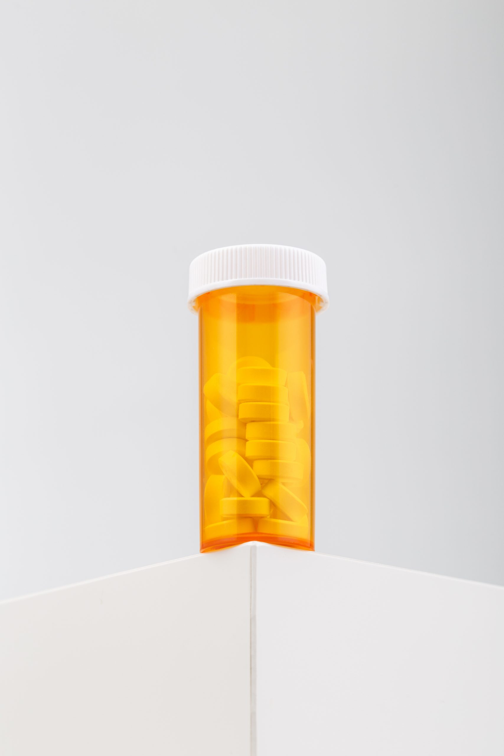 A vertical shot of a yellow container filled with pills on a white table